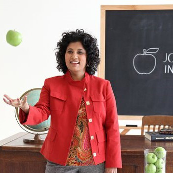 Bhavna tossing a green apple in front of a chalkboard
