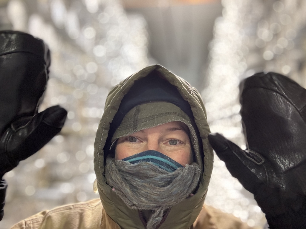 Erika wearing a puffy jacket and gloves and holding up her hands in front of shelves of ice cores.