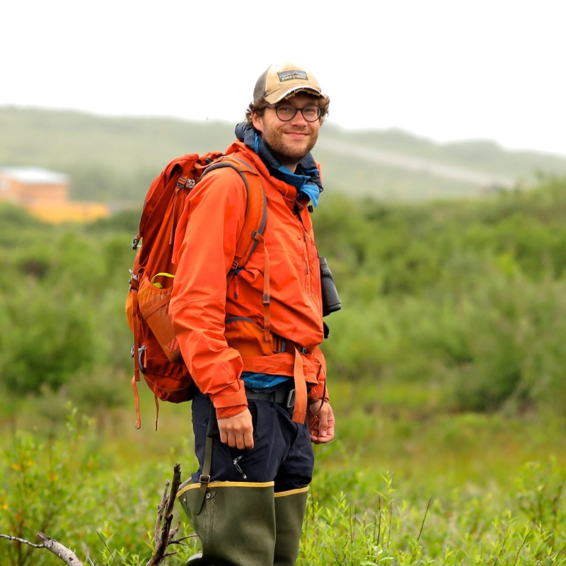 Sebastian in front of a green field and mountains
