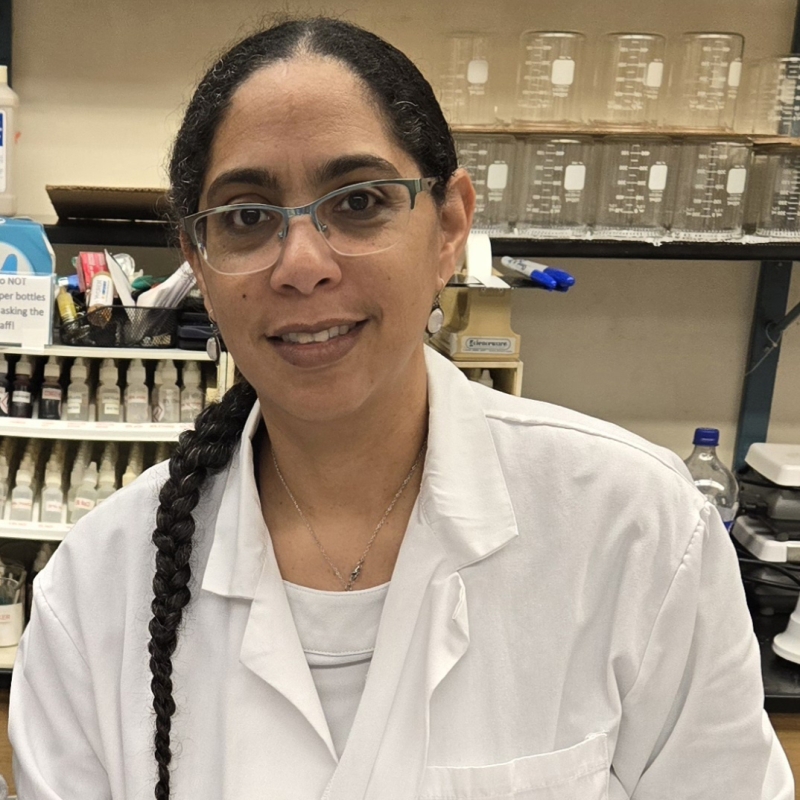 Shakira wearing a lab coat in front of beakers and science equipment
