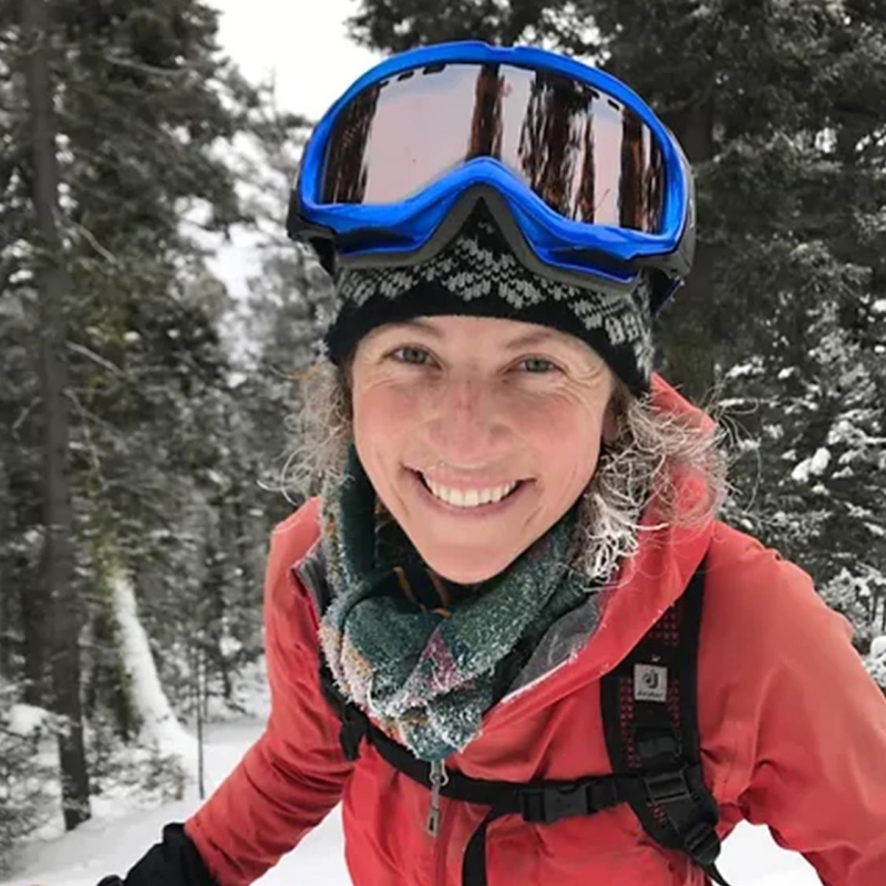 Tracy wearing goggles in front of trees covered in snow