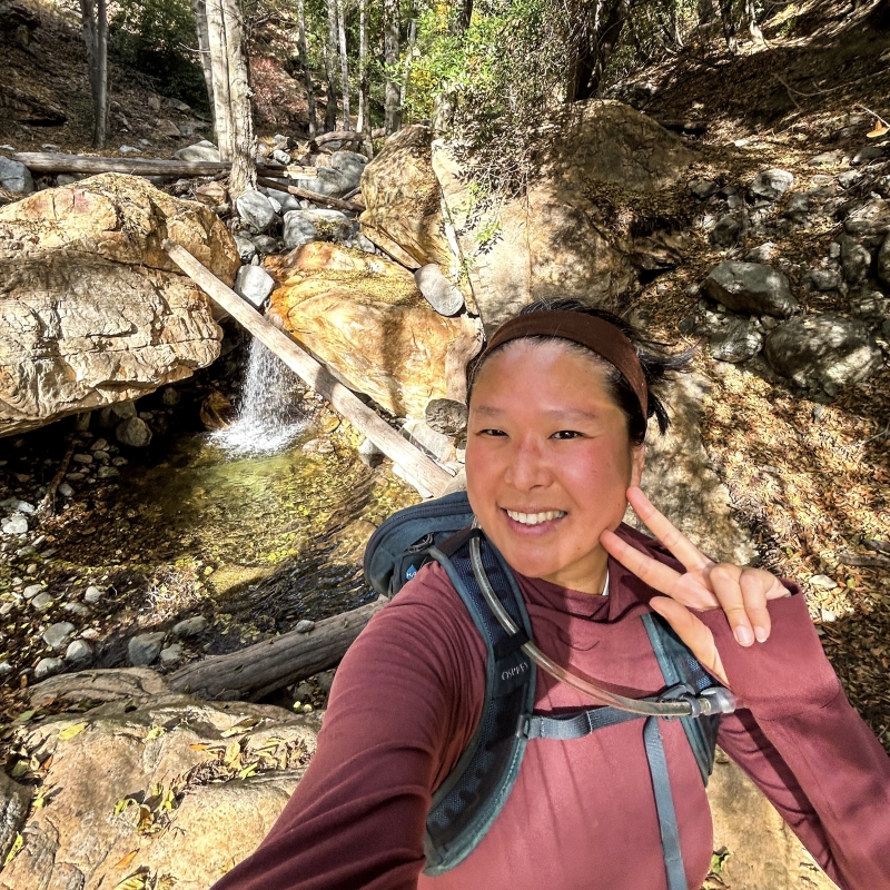 Gail wearing a backpack standing in front of a small waterfall