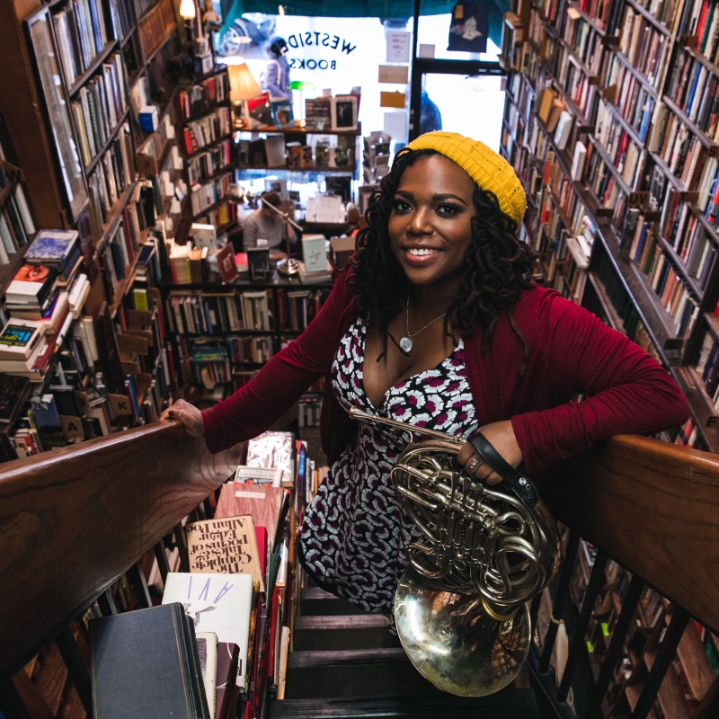 Kyra stands on stairs holding a musical instrument inside of a bookstore