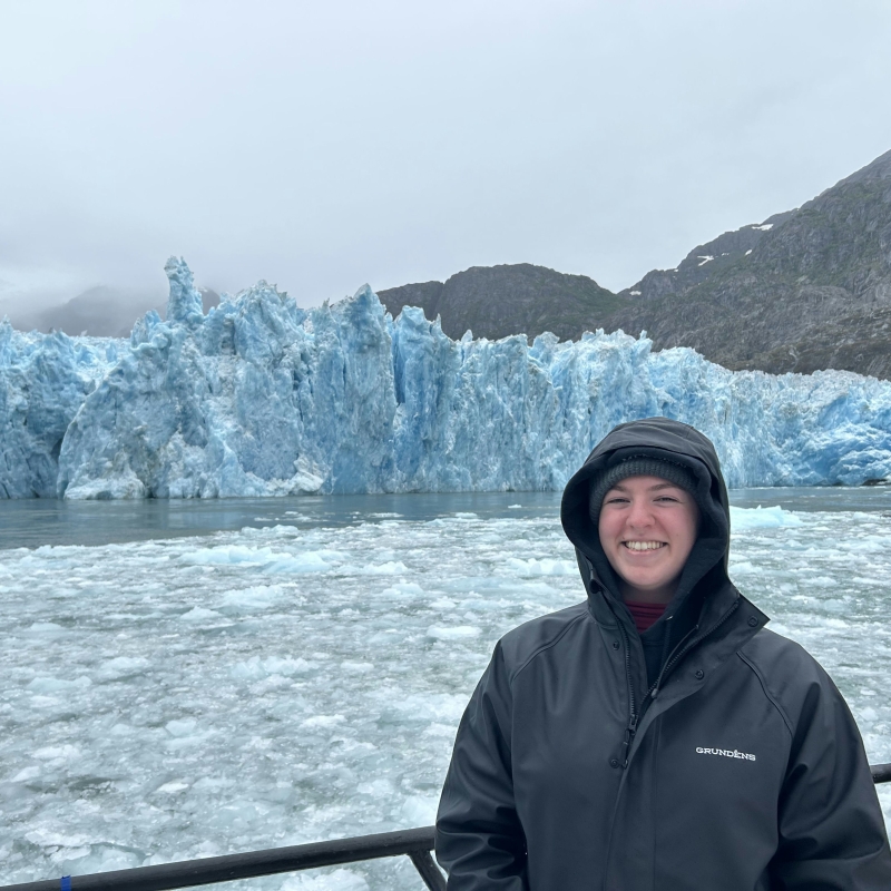 Vanessa stands smiling on a boat in front of a glacier