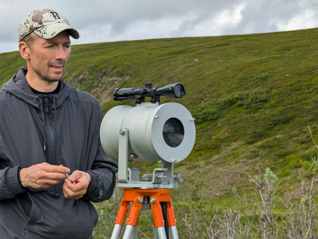 Dr. Aleksey Sheshukov stands next to a piece of equipment with rolling green hills behind him.