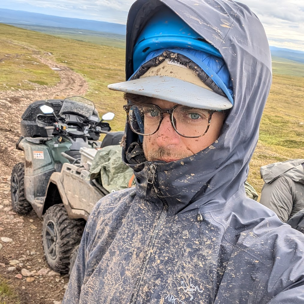 Matt stands in front of an ATV. He is splattered with mud.