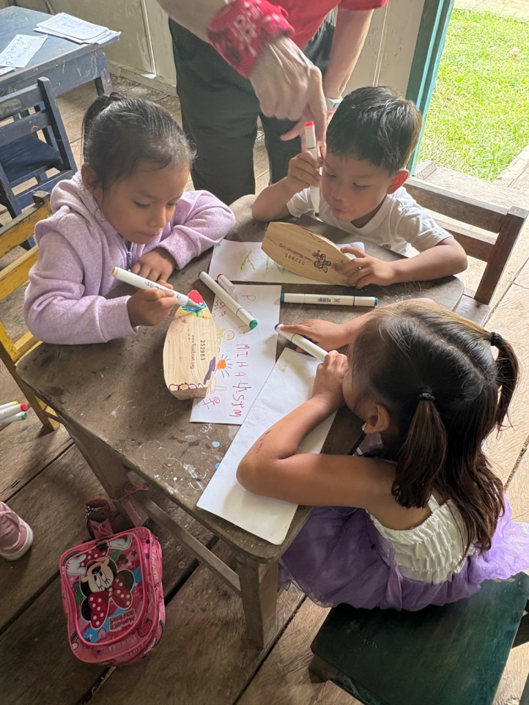 Three kindergarten students decorate a small wooden boat.