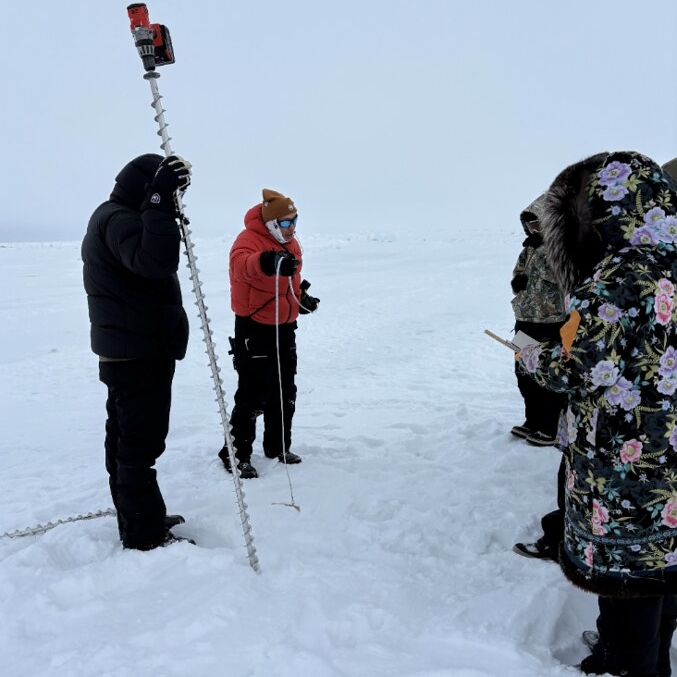 Dr. Ignatius Rigor leading a lesson with 8th graders from Hopson Middle School on the sea ice. Students use an auger to drill small holes and then feed a measuring tape to the ocean floor to measure sea ice depth.