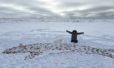 Bethany poses with small decorated wooden boats. The boats have been arranged in the shape of a whale on the snow.