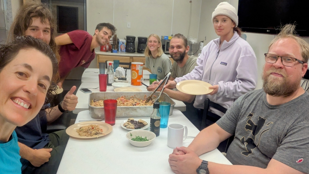 Seven people sit at a table with food