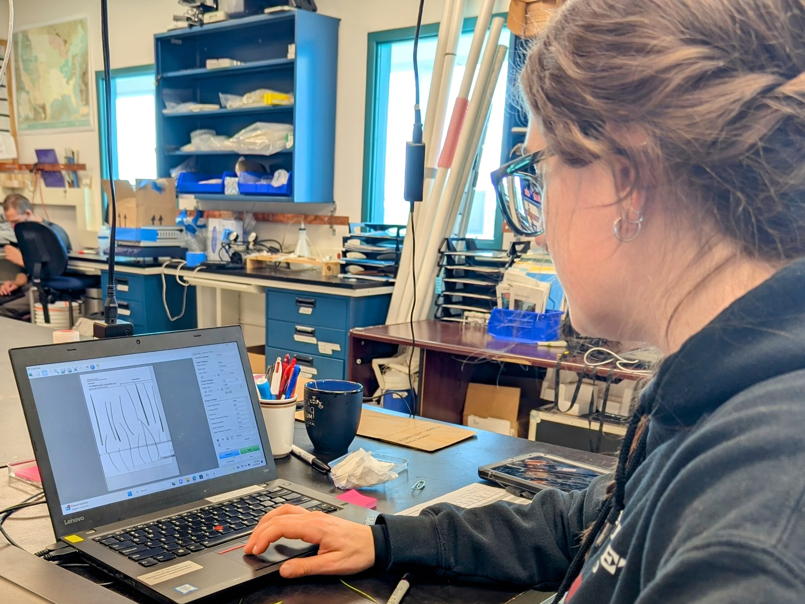 A woman sits at a desk looking at a laptop