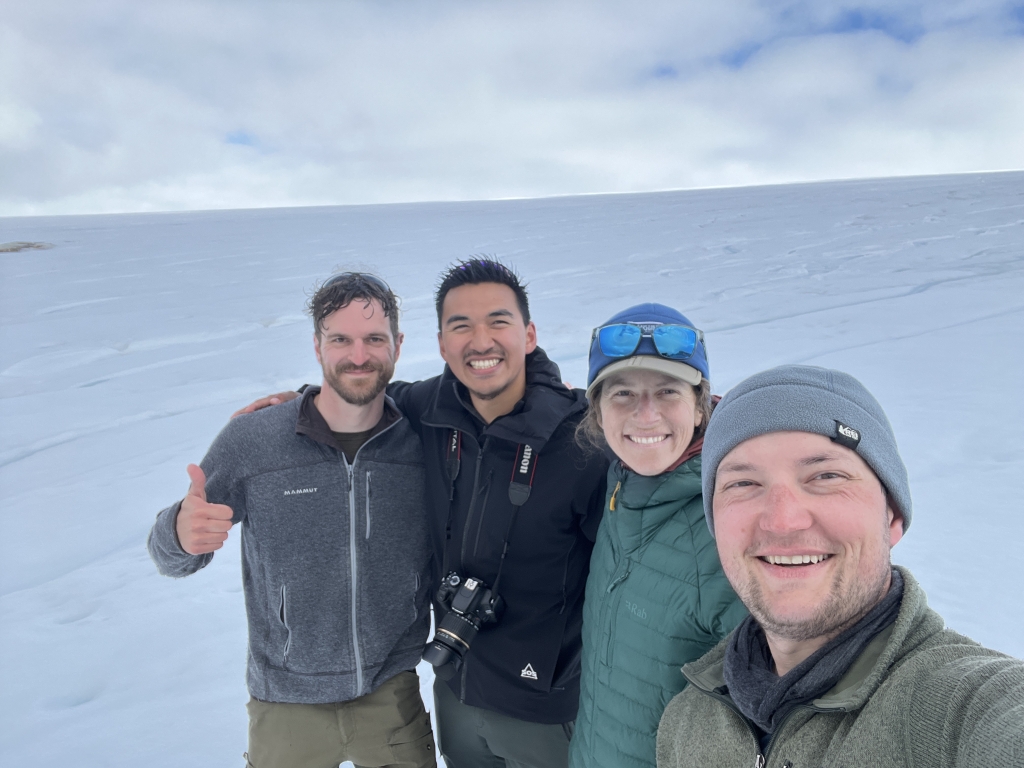 Four people smiling standing in the snow.