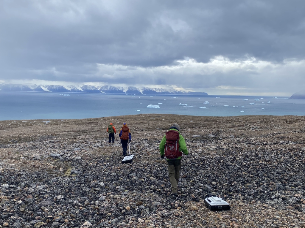 Three people pull machines across rocks as they walk towards the water.