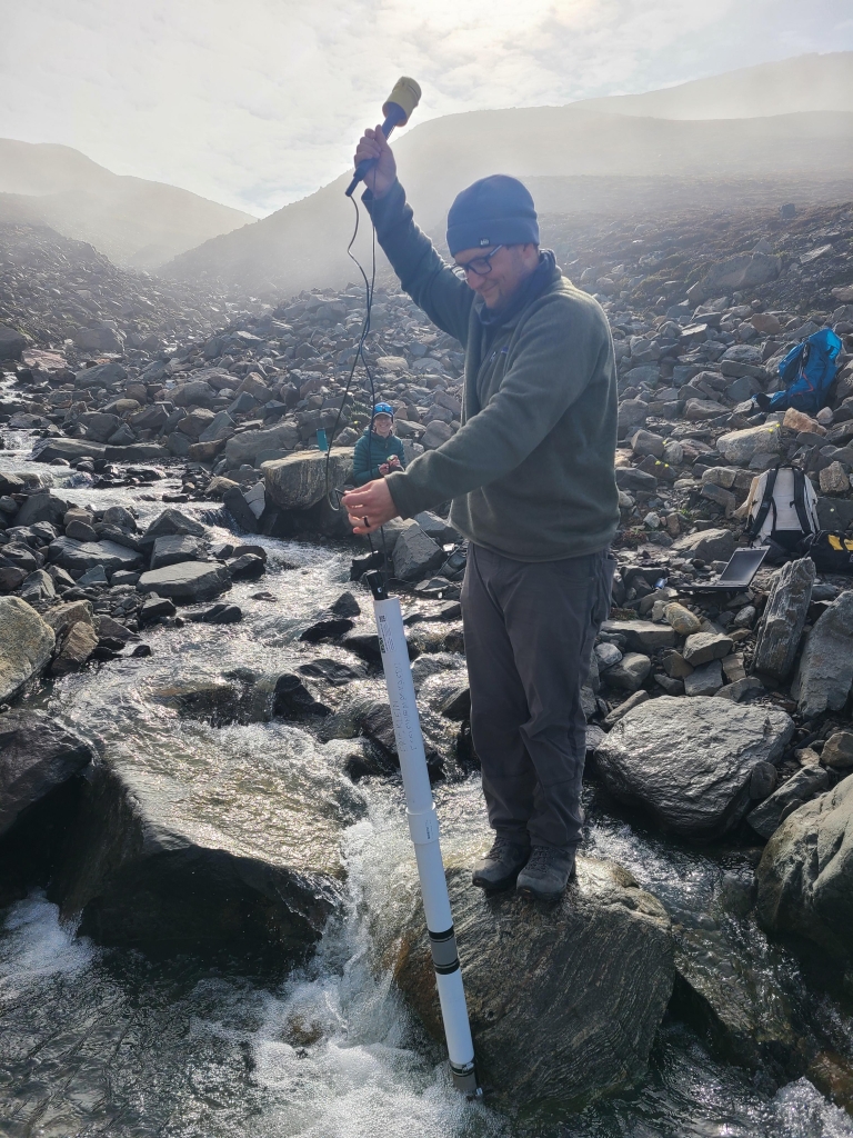 People stand on rocks collecting water samples.