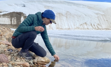 A woman reaches into the stream to collect a water sample