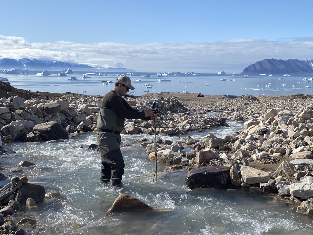 A man stands in a stream holding a meter in the water.