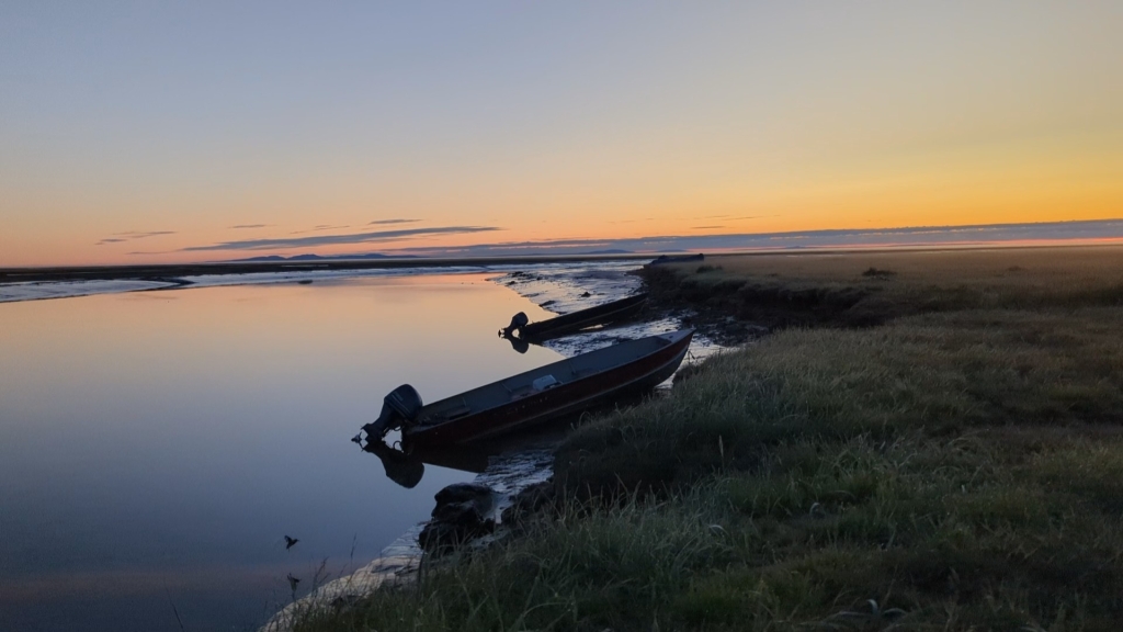 Sunset over two boats sitting on the shore on the edge of the water