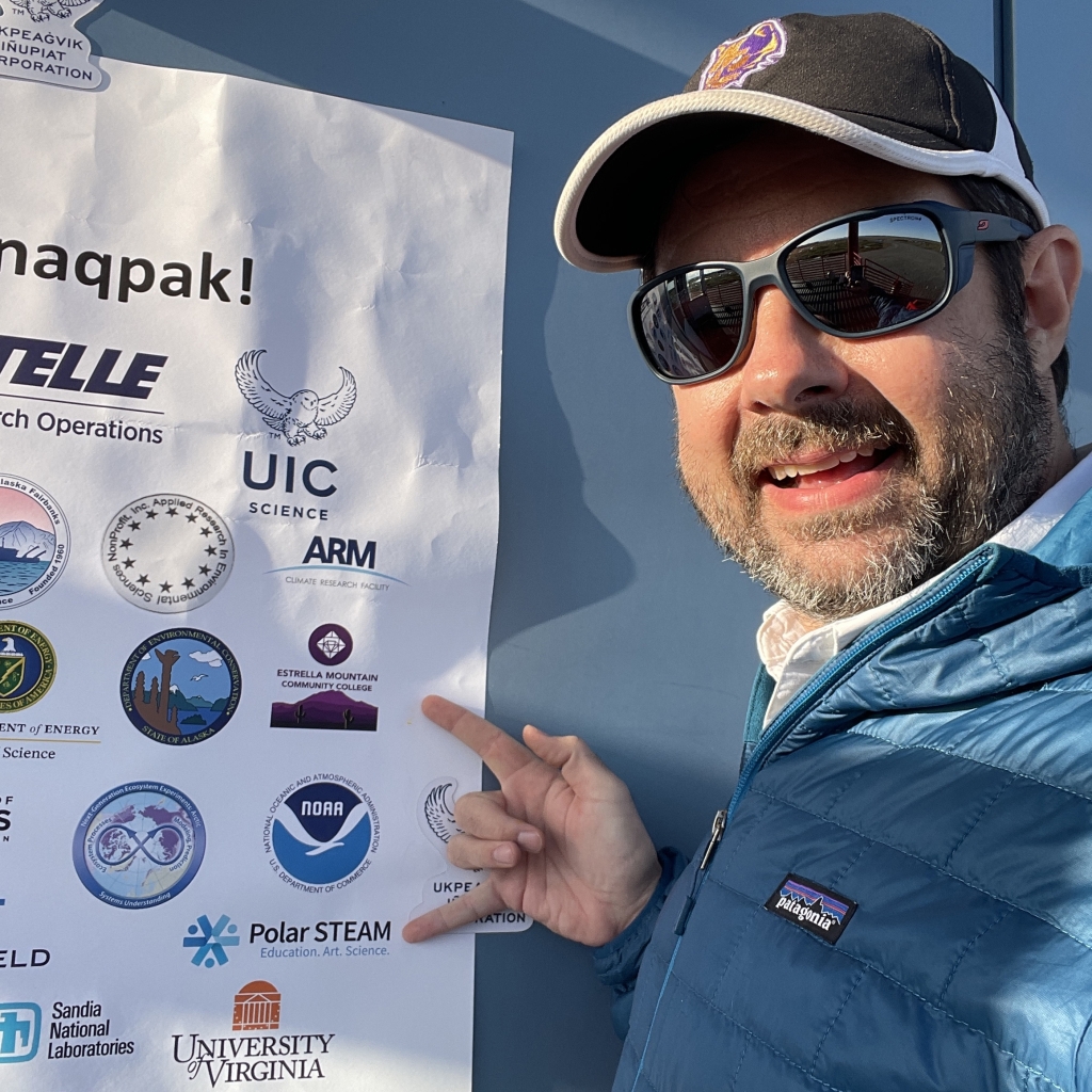 Zachary points to the Estrella Mountain Community College and Polar STEAM logos on a poster