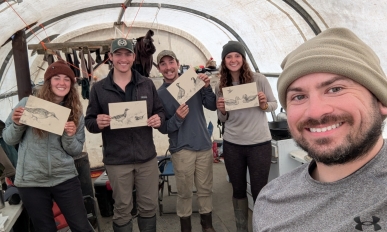 A man smiling at the camera, in the background are four people holding up drawings of birds and smiling