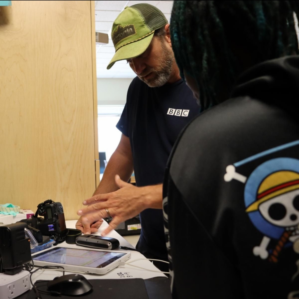 Two people look at a tablet and equipment on a desk