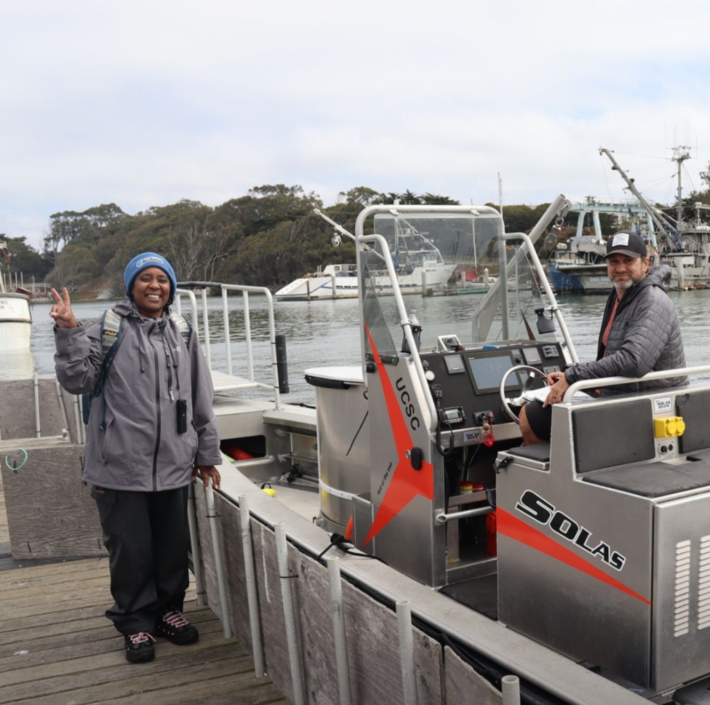 Patt stands next to a boat giving the peace sign