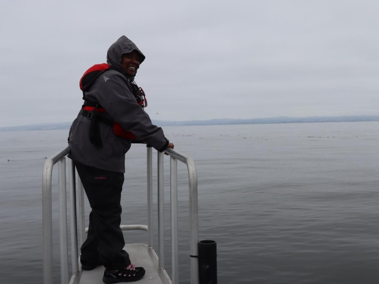A woman stands on a ramp over water looking back and smiling at the camera