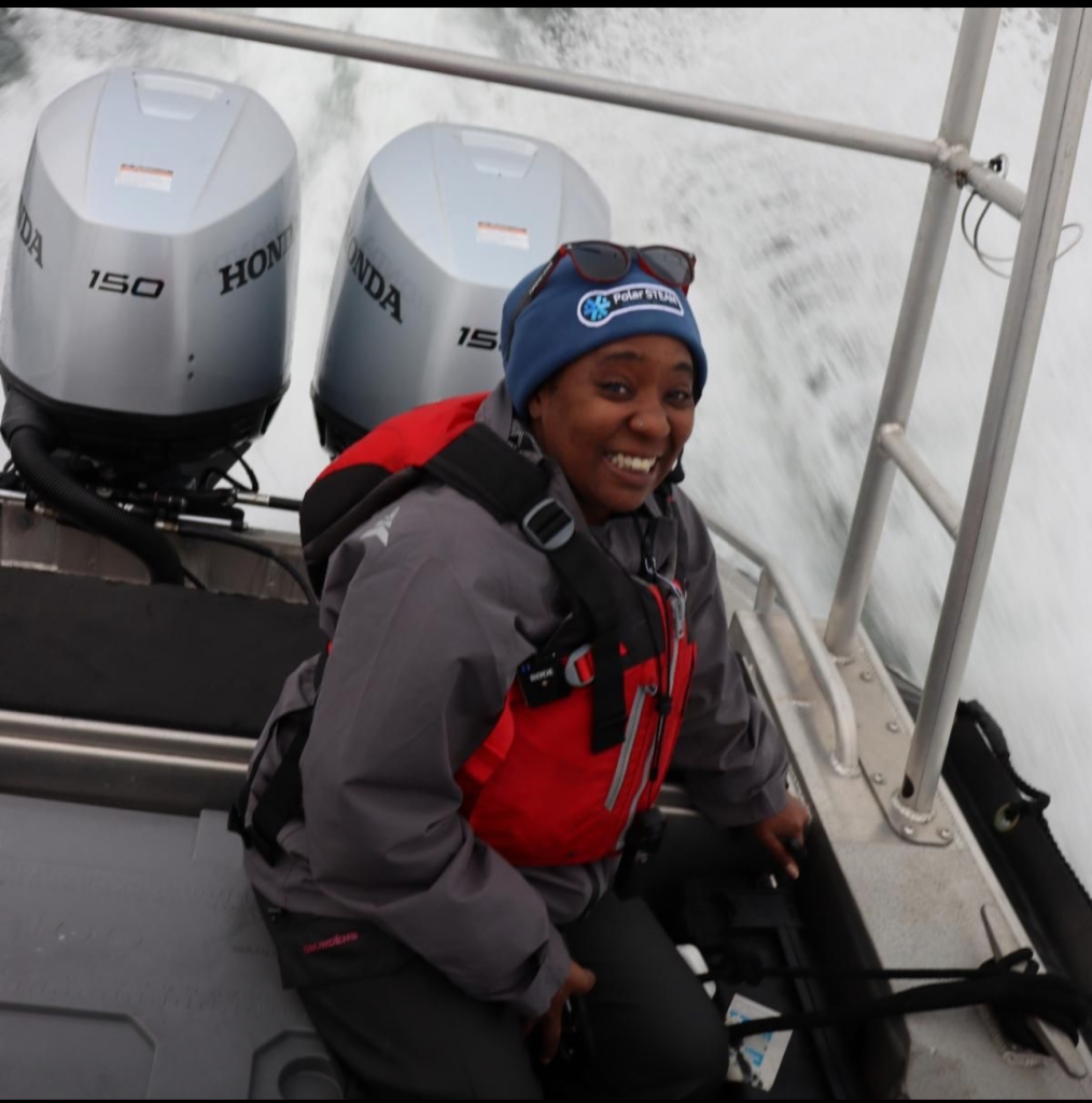 Patt sits on a boat smiling up at the camera
