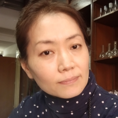 Close up of Chuyon, in the background are shelves that contain beakers