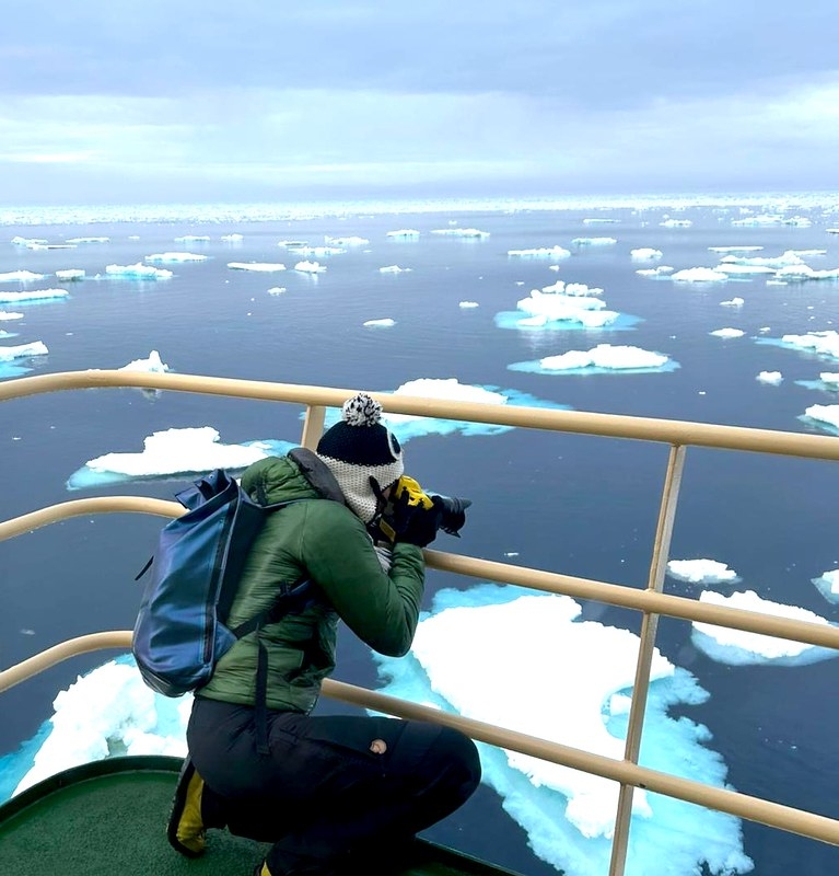 A person crouching near the edge of a ship taking a picture of the water with ice floating in it