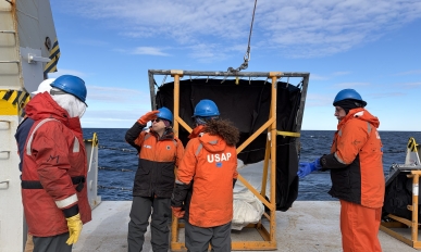 Four people stand next to a big net on the edge of a ship