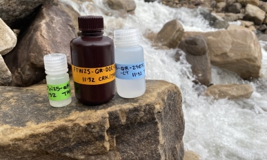 Three bottles of water samples with a waterfall in the background