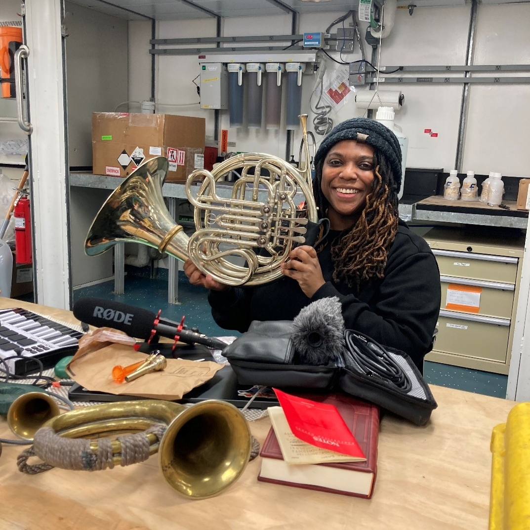 Woman artist holding a french horn in a science lab.