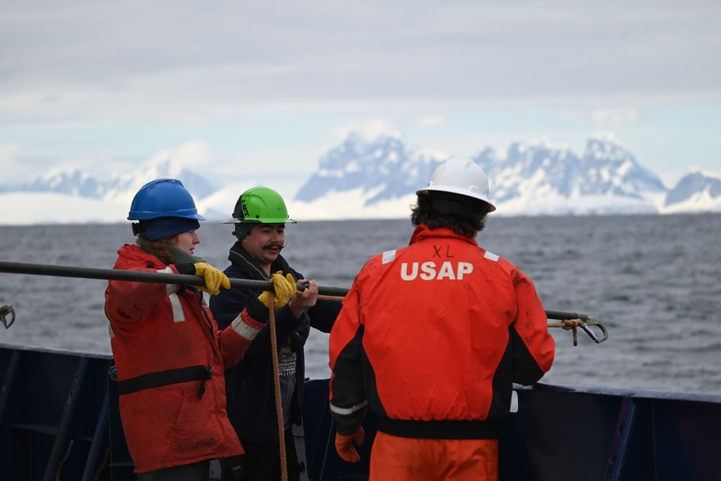 Three people lower a pole with rope attached into water