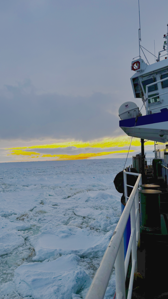 View of a vibrant yellow and orange sunset from a ship with icy water in the foreground