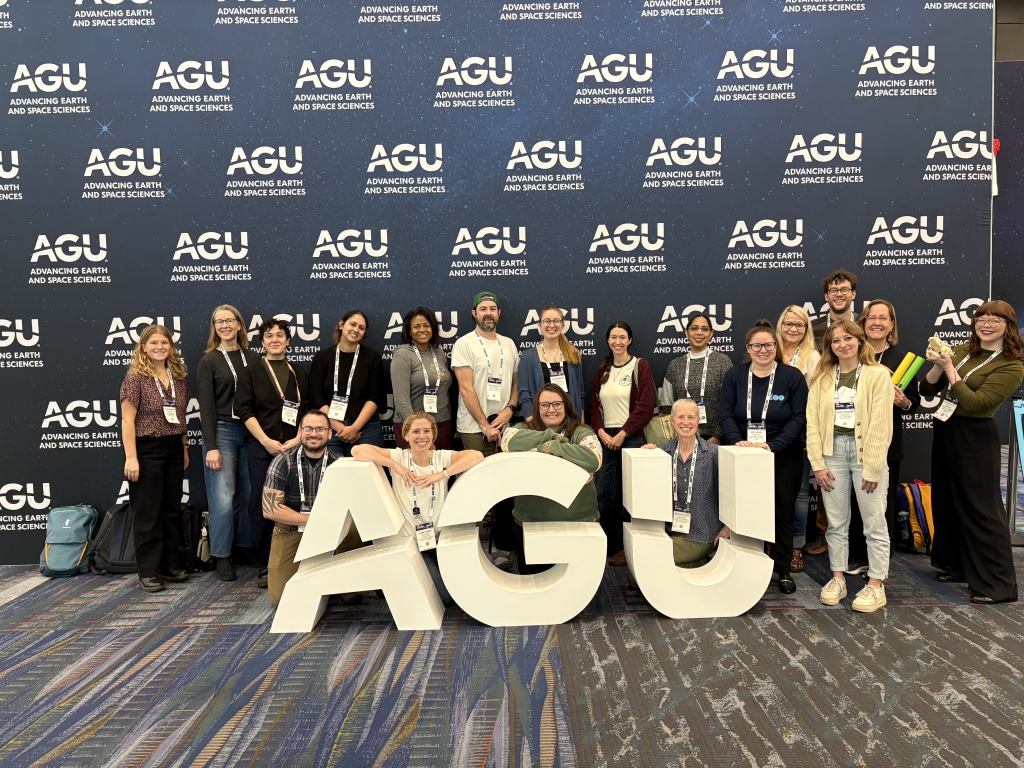 19 Polar STEAM Fellows and team members pose in front of a backdrop that says AGU Advancing Earth and Space Sciences