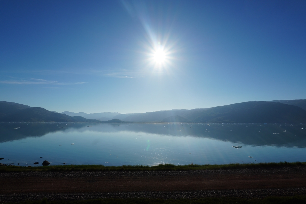 View of the sun over the calm waters of a fjord