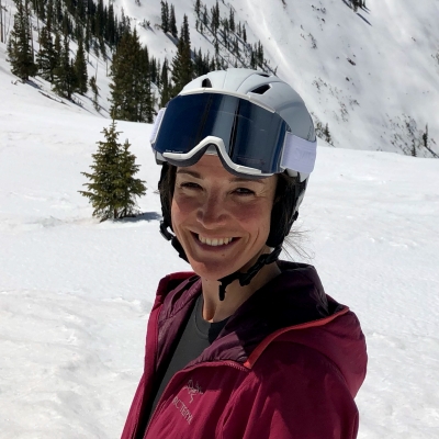 Ali wearing a helmet and goggles in front of a snowy mountain