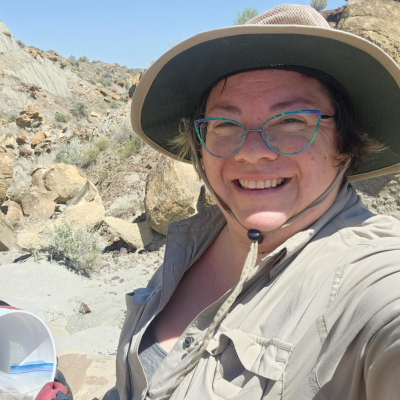 Michelle wearing a hat and glasses in front of a rocky landscape