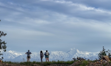 Silhouette of three people looking at a mountain range in the distance.