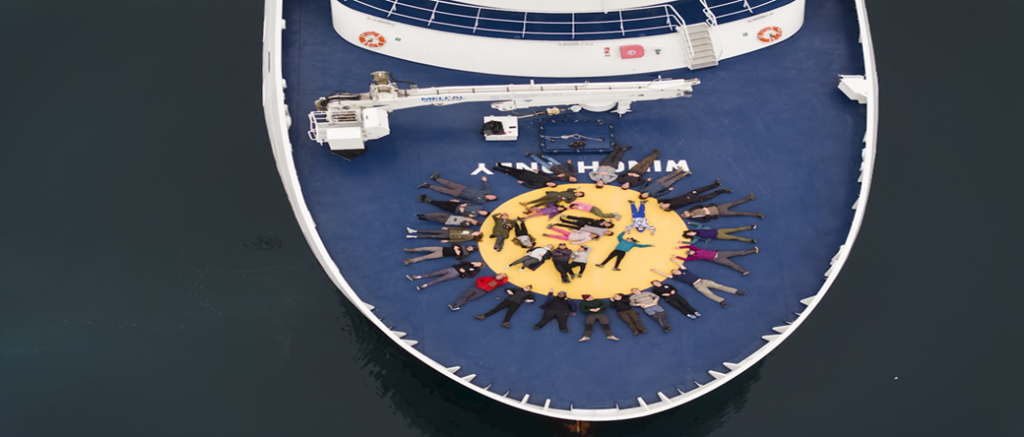 Sky view of a group of people laying on the deck of a ship in a circle looking up at the sky