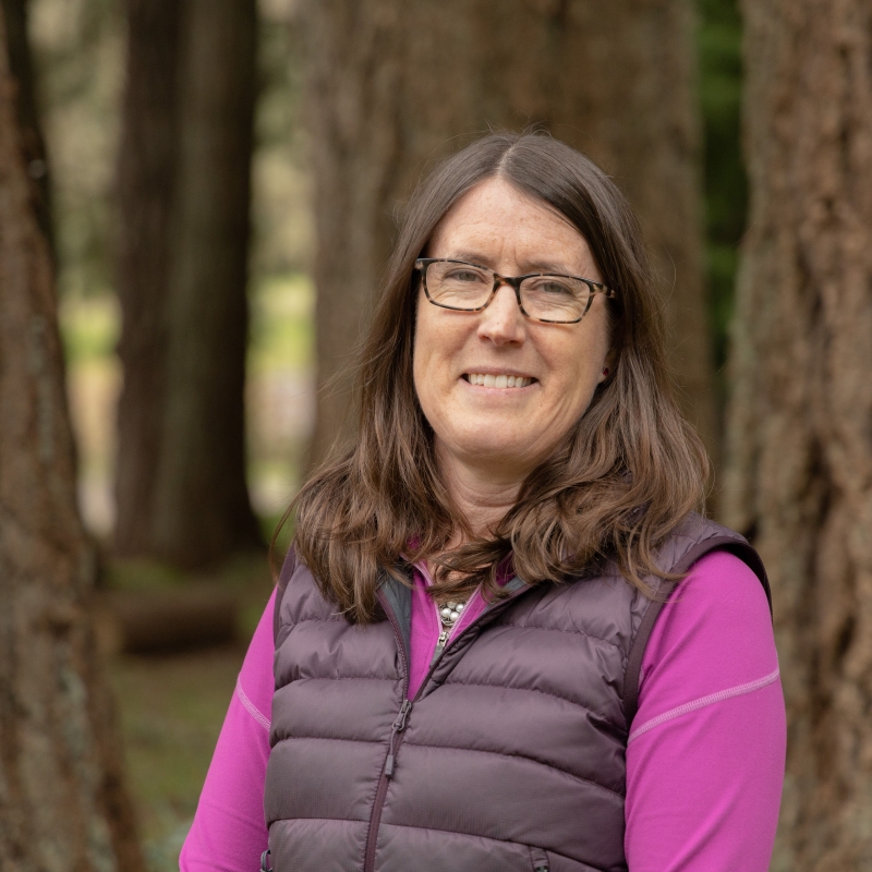 Kari smiling in front of a background of trees