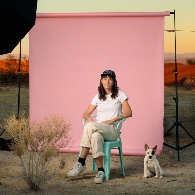 Margeaux sitting in front of a pink background set up in a dessert landscape. There is a small dog sitting nearby.
