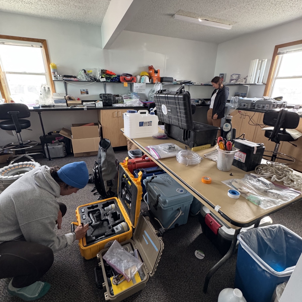 Two people packing equipment in an office with supplies scattered everywhere