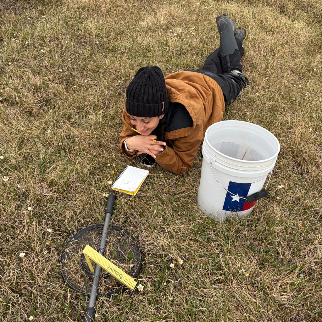 Lauren lays on the grass with a notebook looking at some equipment