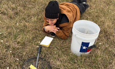 Lauren lays on the grass with a notebook looking at some equipment