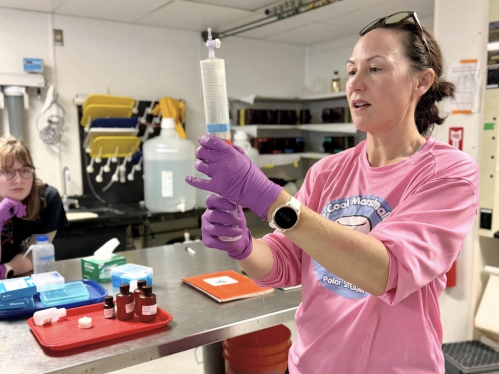 A person wearing gloves holds up and looks at a syringe containing a water sample