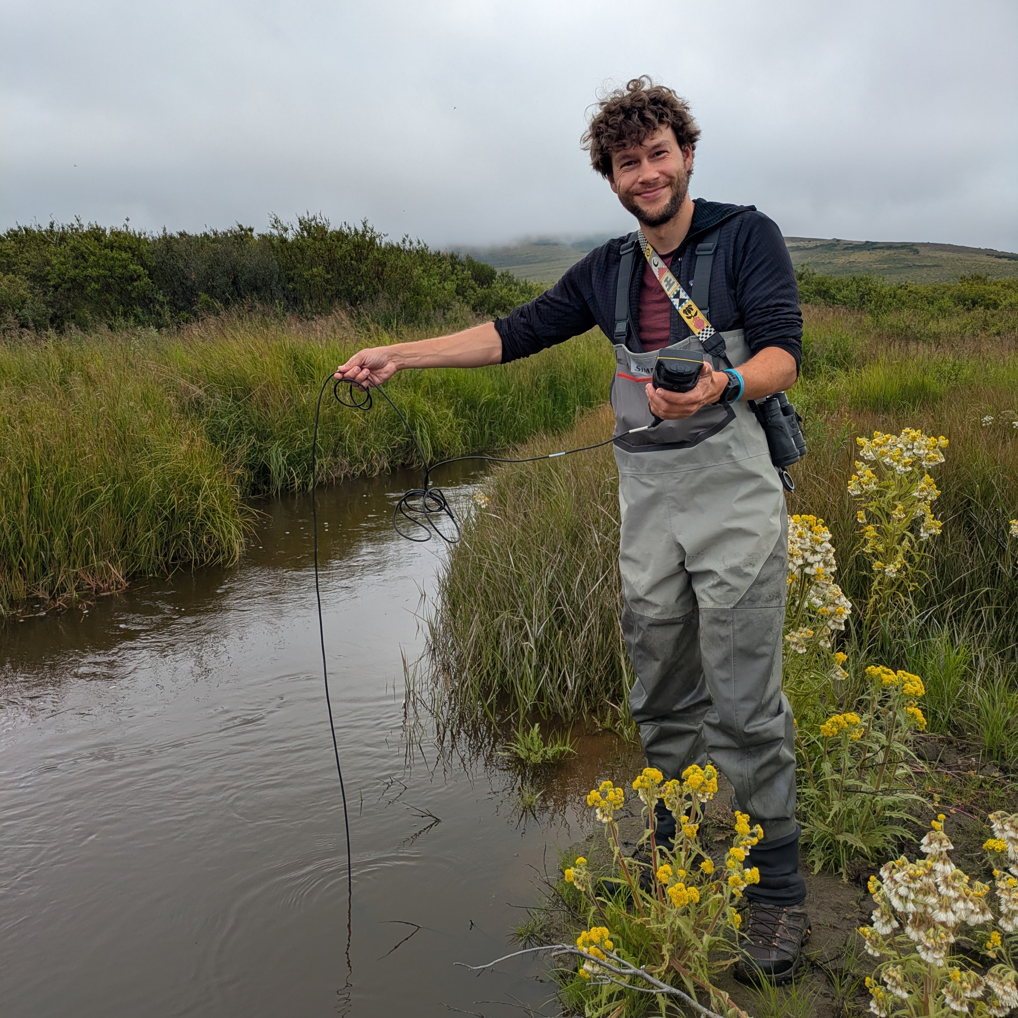 Picture of a man holding a cord, which is submerged in a stream.
